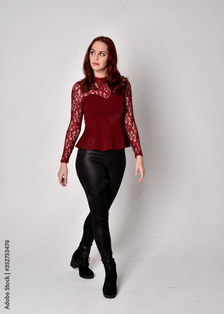 Portrait of a pretty girl with red hair wearing leather pants and long sleeved lace shirt. full length standing pose, isolated against a studio background. Portrait of a pretty girl with red hair wearing leather pants and long sleeved lace shirt. full length standing pose, isolated against a studio background.