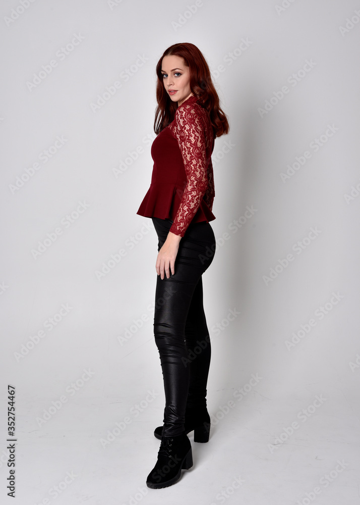 Portrait of a pretty girl with red hair wearing leather pants and long sleeved lace shirt. full length standing pose, isolated against a studio background. Portrait of a pretty girl with red hair wearing leather pants and long sleeved lace shirt. full length standing pose, isolated against a studio background.