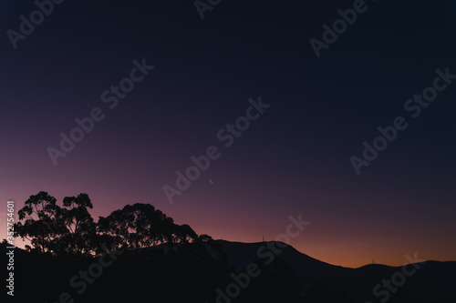 sunset sky with blue to purple to orange gradient colors (unedited) and moon over the hills with eucalyptus tree silhouettes