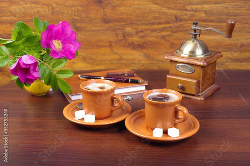 Two cups of coffee  notebook  pen  flash drive  coffee grinder  rose hip flower on a wooden table.