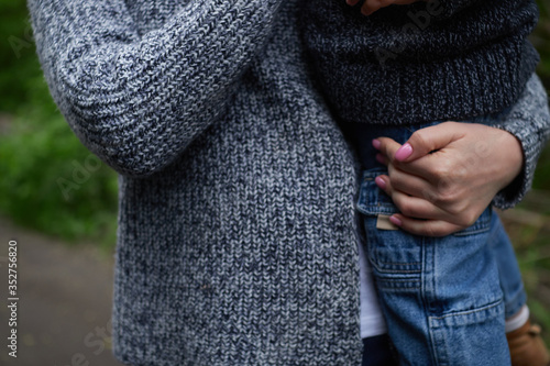mother in a dark blue knitted sweater holds a child in jeans in her hands walking through the summer park close-up