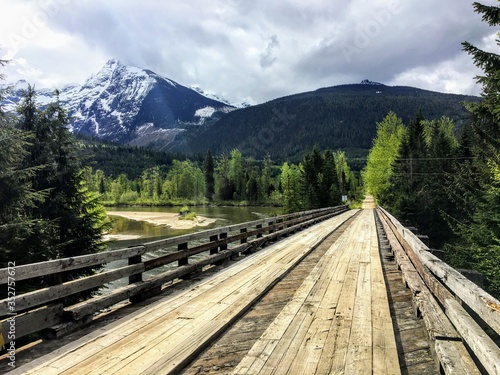 a wooden bridge with the mountains and forest in the background © christopher