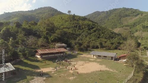 Aerial shot of people in village against green mountains, drone flying backward over valley on sunny day - Mekong River, Laos photo