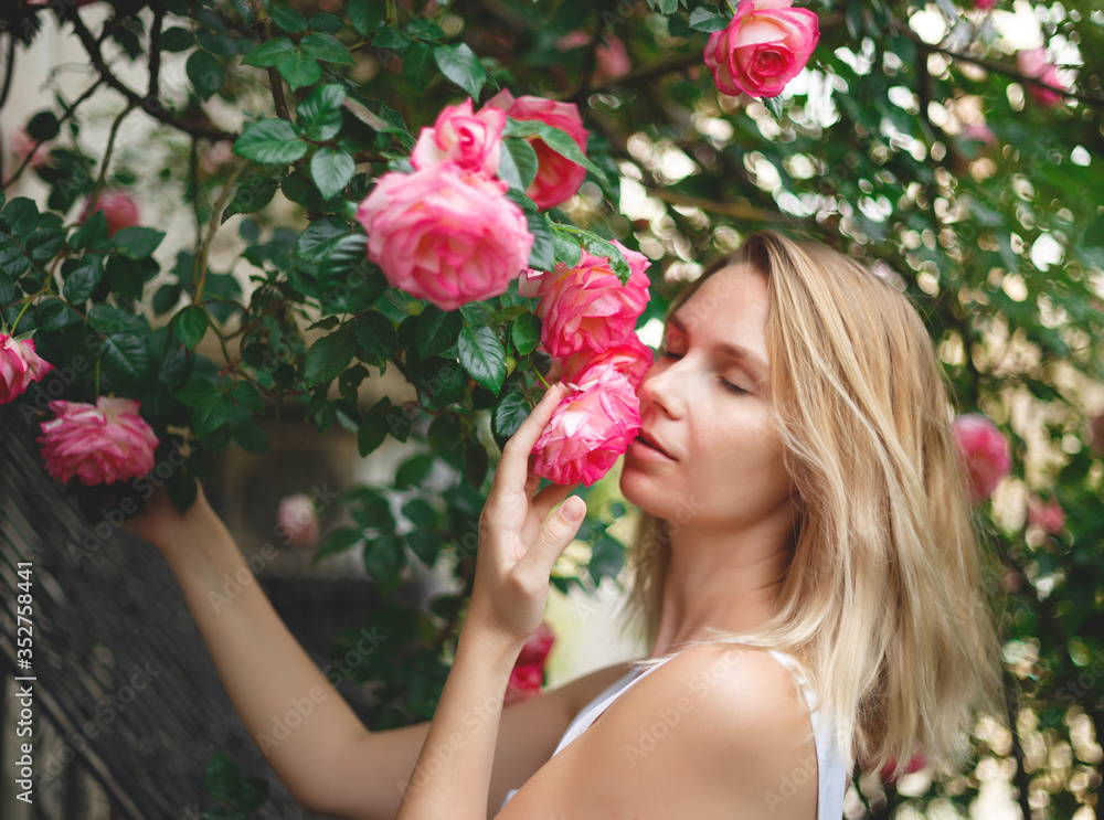 blond woman smiling in a flowering bush of pink roses blond woman smiling in a flowering bush of pink roses