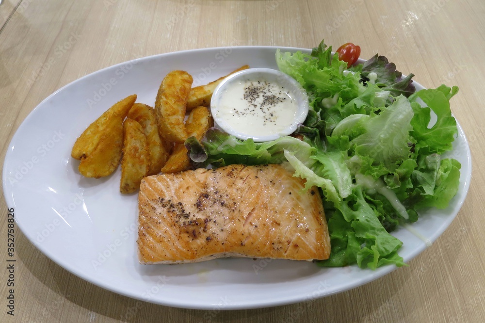 Grilled salmon garnished, roasted salmon steak, with cooked potatoes and sauce on white plate. Food concept. Grilled salmon garnished, roasted salmon steak, with cooked potatoes and sauce on white plate. Food concept.