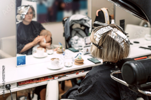 Young woman in beauty salon coloring her hair together with her baby. Selective focus