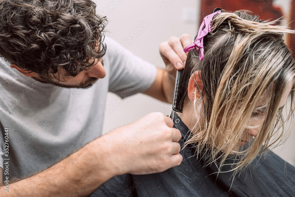 Fototapeta premium Master hairdresser cuts hair of blond woman in salon. Close up photo. Selective focus.