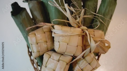 Cinematic shot of popular Malay traditional food, Ketupat rice and Lontong Nasi Impit in one basket. Ketupats, a natural rice casing made from young coconut leaves for cooking rice. Slow motion video. photo