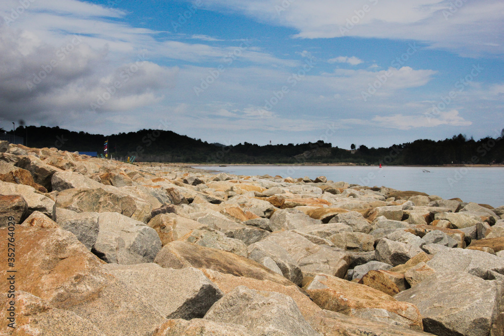 rocky coastline with low mountainous tree filled horizon under a cloudy blue sky. calm ocean near wave breaking rocky beach. rocky coastline with low mountainous tree filled horizon under a cloudy blue sky. calm ocean near wave breaking rocky beach.