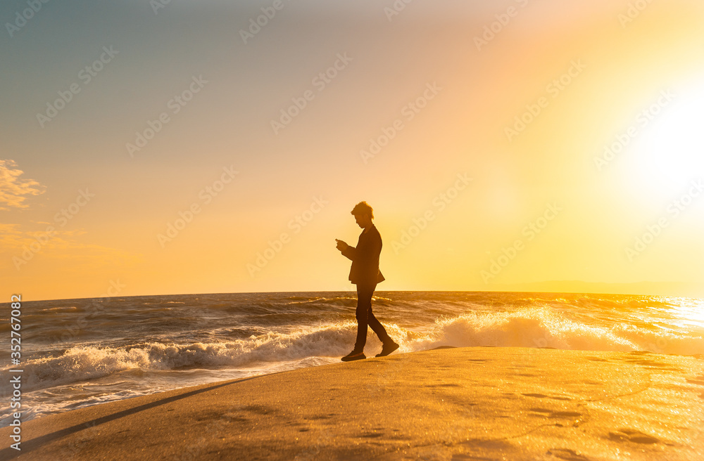 日本 神奈川県 鎌倉の七里ヶ浜の砂浜を夕方に歩く若い日本人男性と美しい夕陽