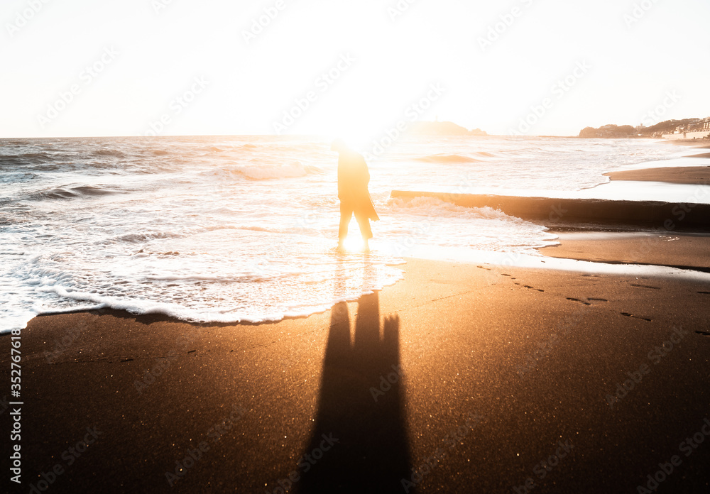 Φωτογραφία 日本 神奈川県 鎌倉の七里ヶ浜の砂浜を夕方に歩く若い日本人男性と美しい夕陽