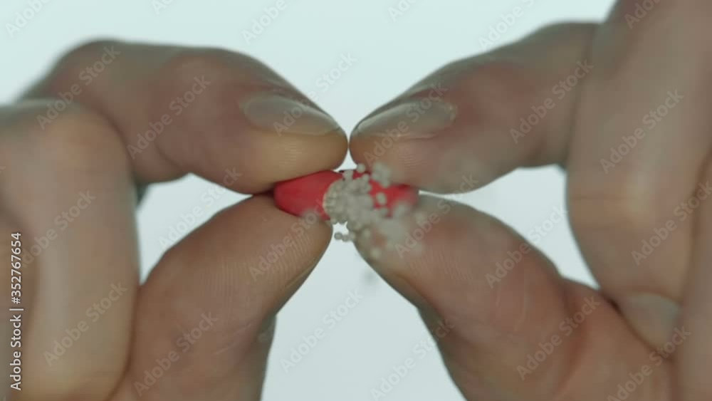 A man opens a red medical capsule and spills white powder from it directly into the camera on a white background. Closeup. Slow motion. High speed camera A man opens a red medical capsule and spills white powder from it directly into the camera on a white background. Closeup. Slow motion. High speed camera