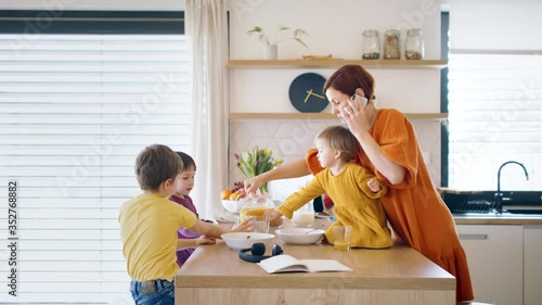Mother with small children and smartphone in kitchen in the morning at home, eating breakfast.