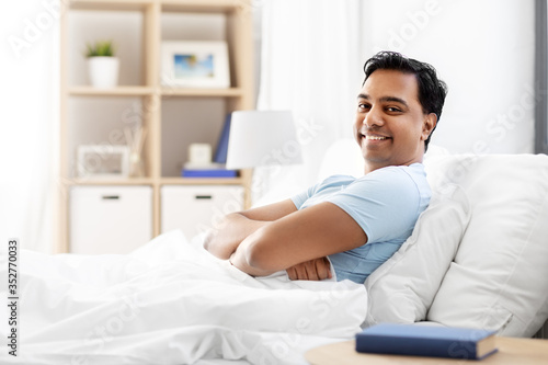 people, bedtime and rest concept - happy smiling indian man lying in bed at home