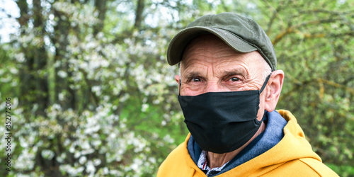 senior man in cap black mask looks ahead in garden closeup