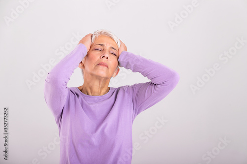Mature woman holding her head with her hands while having a headache and feeling unwell. Senior woman with headache, pain face expression. Elderly woman having head pain migraine © Graphicroyalty
