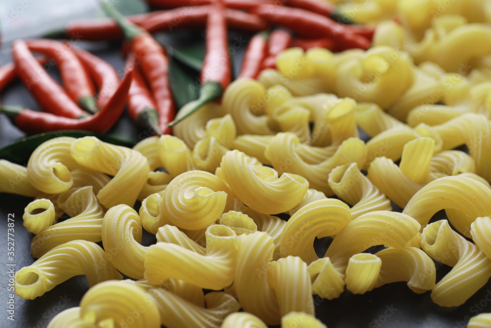 Uncooked pasta on a stone background. With seasonings and spices, spicy chili peppers.