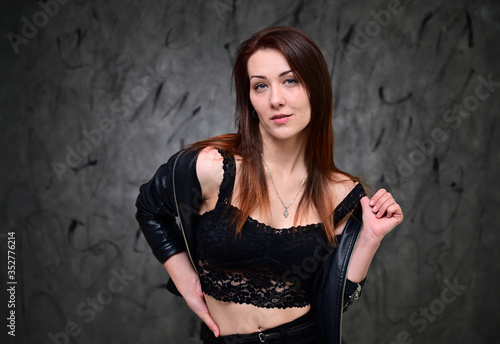 A pretty model is standing on a gray background in a black jacket. Studio portrait of a caucasian brunette girl with minimal makeup.