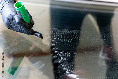 close up of a professional cleaneer using a diamond blade scraper to clean a window photo