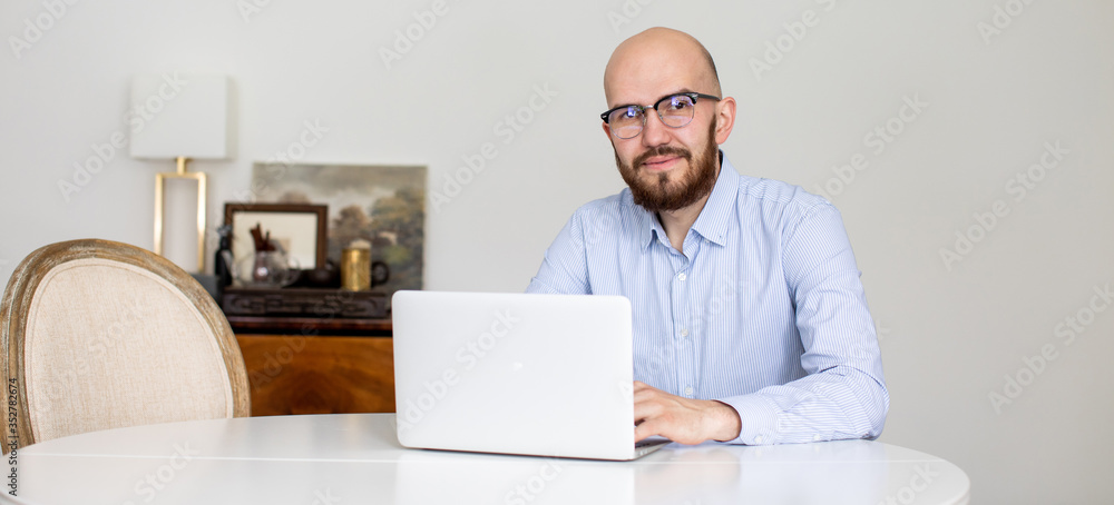 A man with glasses is working on a laptop in his bright living room A man with glasses is working on a laptop in his bright living room