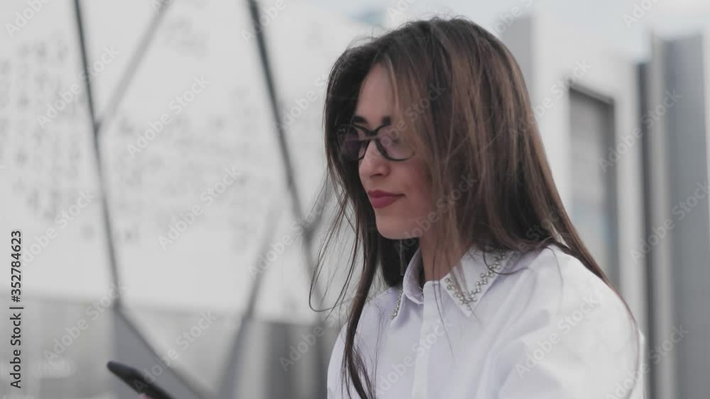 Beautiful businesswoman in glasses talking on smartphone and drinking coffee while sitting in the park near her office Beautiful businesswoman in glasses talking on smartphone and drinking coffee while sitting in the park near her office