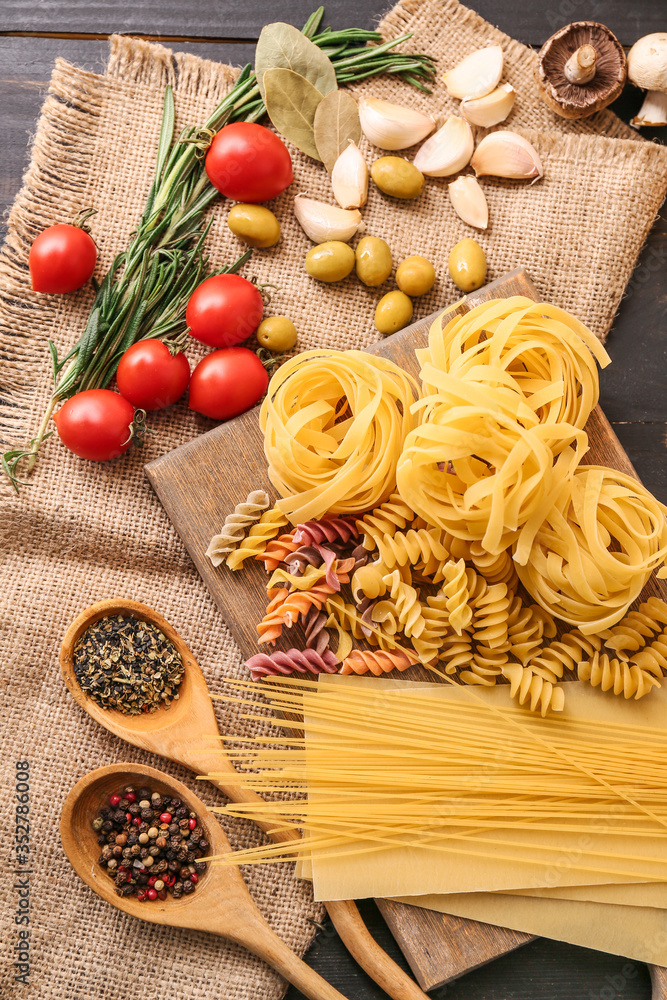 Different uncooked pasta with spices and vegetables on table Different uncooked pasta with spices and vegetables on table