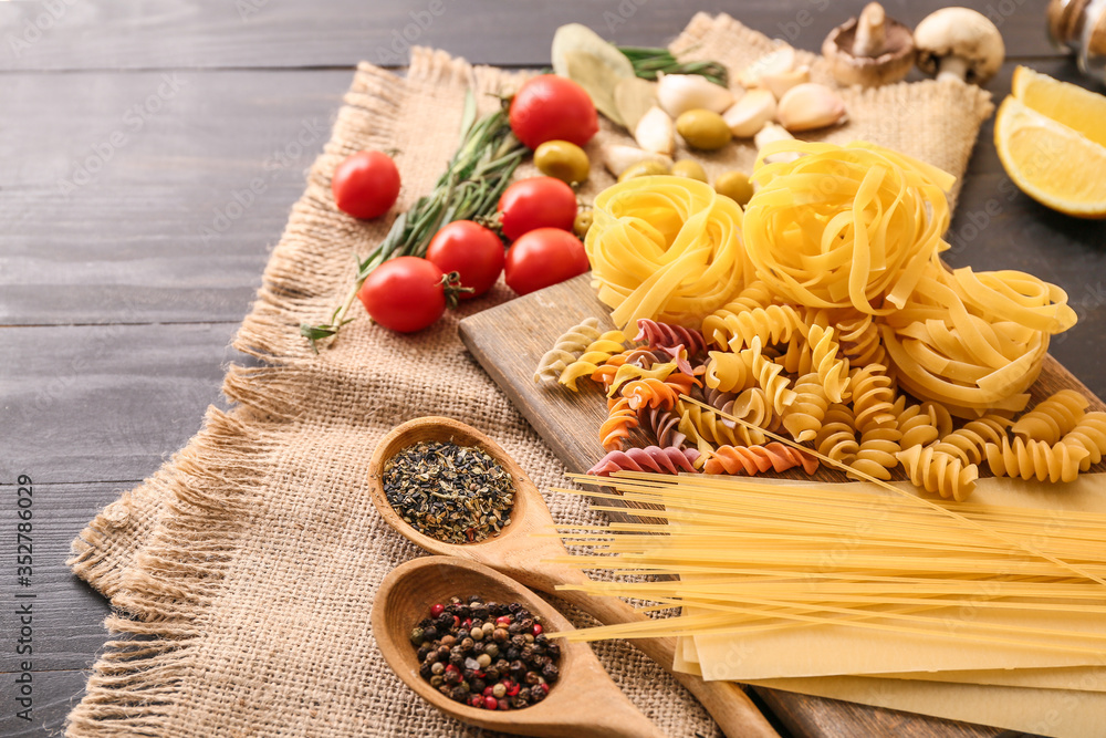 Different uncooked pasta with spices and vegetables on table