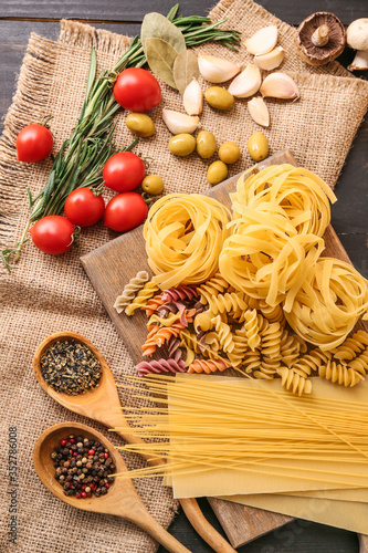 Different uncooked pasta with spices and vegetables on table