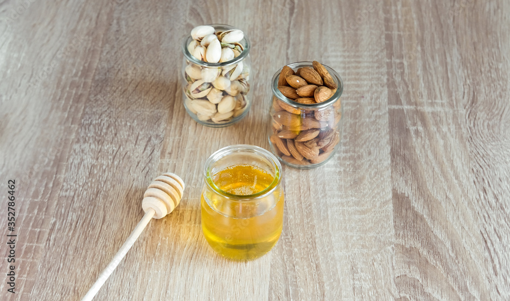 Honey in glass jar with wooden honey dipper and almonds, peanuts on light wooden table background. Honey in glass jar with wooden honey dipper and almonds, peanuts on light wooden table background.