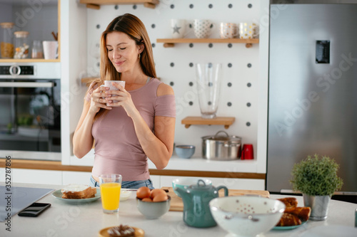 Beautiful woman drinking coffee in the kitchen. Young woman enjoy at home.