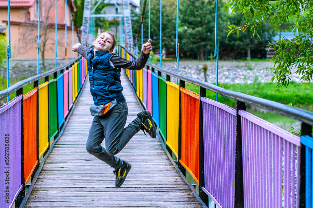 Happy boy in a joy jump on a bridge painted in rainbow colors. End of quarantine coronavirus COVID-19. Holidays. Travels. Freedom of movement. Summer time. Spring time. Happiness