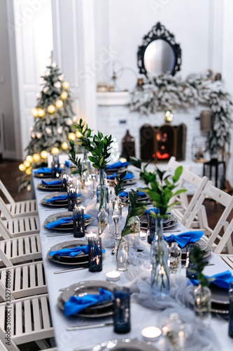 White living room with long served table  fireplace and christmas tree. Cozy atmosphere for celebration. Concept of trendy combination.