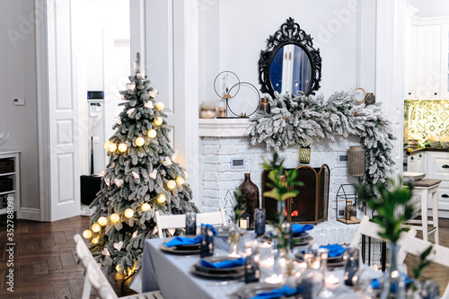 Beautiful living room with fireplace, christmas tree and festive table. Christmas decoration in classic blue and white colors. © Tymoshchuk
