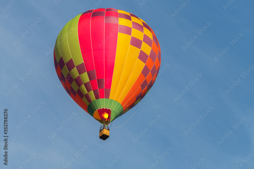 Naklejka premium Colorful hot air balloon on an early morning flight at Canberra, Australia. With an isolated blue sky backdrop with copy space for text.