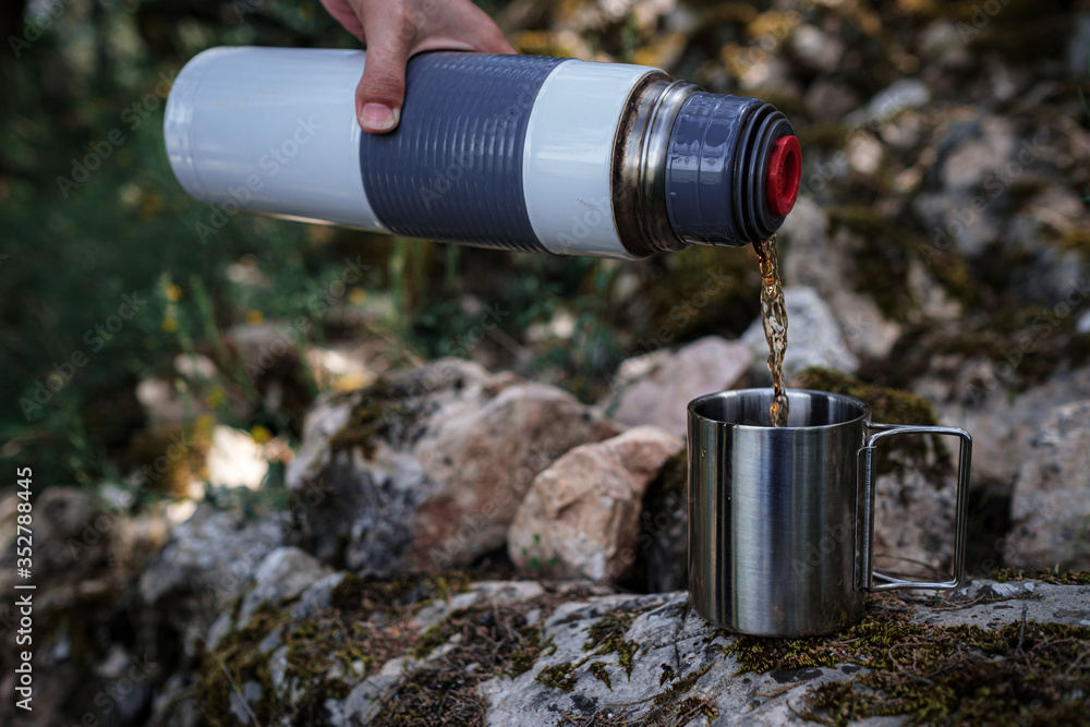 In a camping mug pours tea from a thermos in nature. In a camping mug pours tea from a thermos in nature.