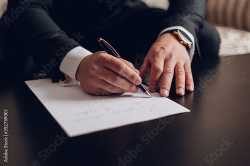 Εκτύπωση καμβά Businessman in dark suit and blue shirt sitting at office desk signing a contract with shallow focus on signature