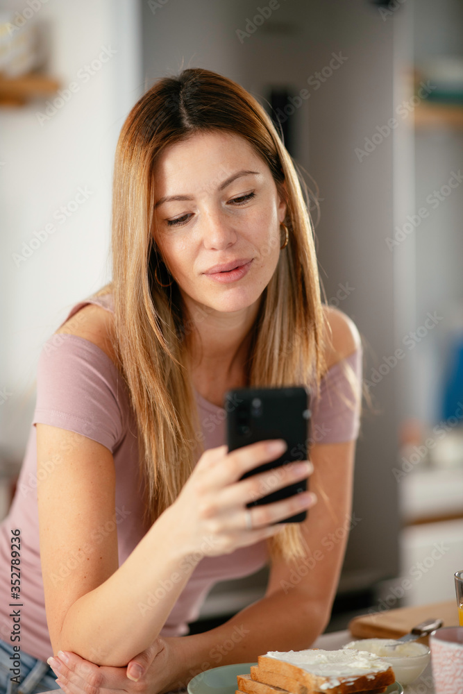 Beautiful woman drinking orange juice in the kitchen. Young woman reading the news online. Beautiful woman drinking orange juice in the kitchen. Young woman reading the news online.