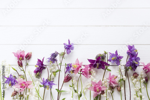 Flowers flat design. Floral composition with pink and purple Aquilegia and Convallaria flowers. Template with copy space on white wooden board