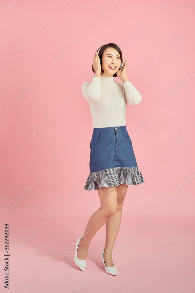 Full length image of pleased african woman dancing and listening music by the smartphone while looking at the camera over pink background Full length image of pleased african woman dancing and listening music by the smartphone while looking at the camera over pink background