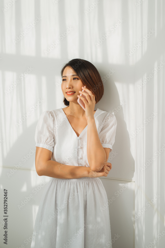 Young Asian woman talking on smartphone against white wall Young Asian woman talking on smartphone against white wall