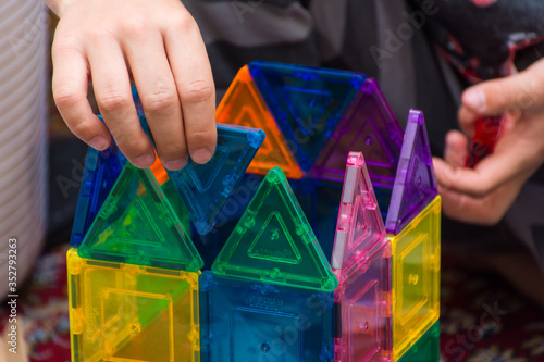 Young child building geometric magnetic shapes into a creative building at home indoors for education, problem solving, fun, enjoyment and leisure.