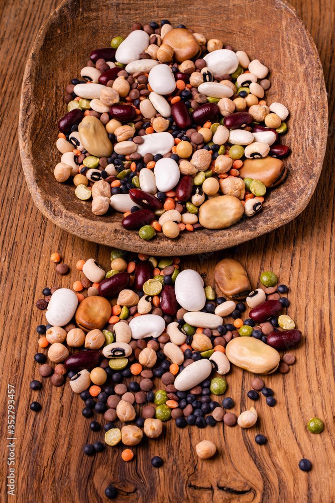 in the foreground, varieties of dried legumes mixed in a large spoon and on a rustic wooden background