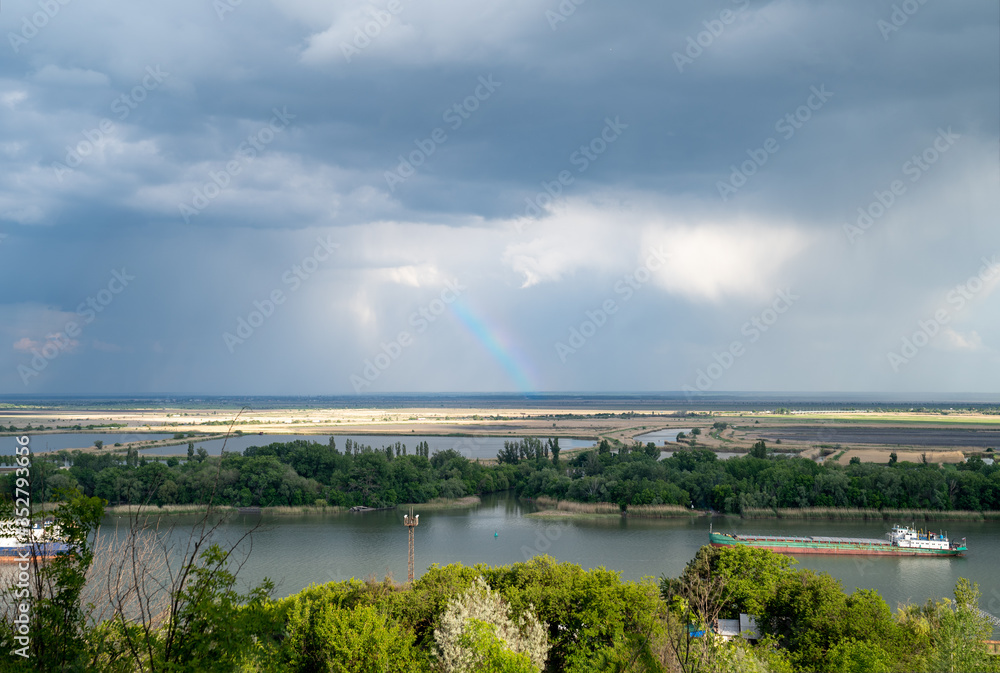 rainbow in the sky over the river, barges are anchored.