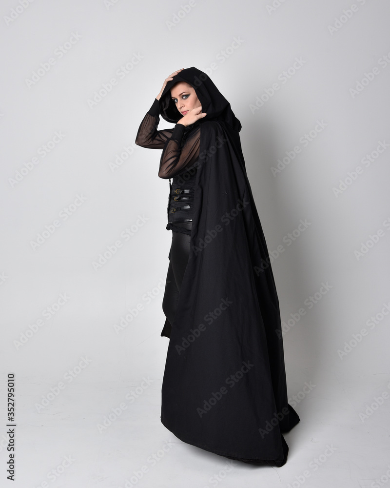 fantasy portrait of a woman with red hair wearing dark leather assassin costume with long black cloak. Full length standing pose in side profile isolated against a studio background. fantasy portrait of a woman with red hair wearing dark leather assassin costume with long black cloak. Full length standing pose in side profile isolated against a studio background.