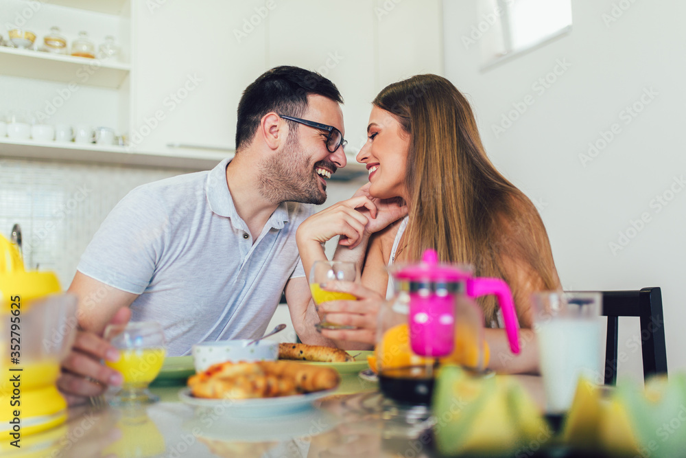Young happy couple sitting in modern apartment and having breakfast together.