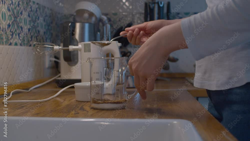Woman cooking Dalgona coffee closeup. Instant coffee and sugar in a beaker. Close up female hands pouring water there, and whipping coffee with a mixer. Woman cooking Dalgona coffee closeup. Instant coffee and sugar in a beaker. Close up female hands pouring water there, and whipping coffee with a mixer.