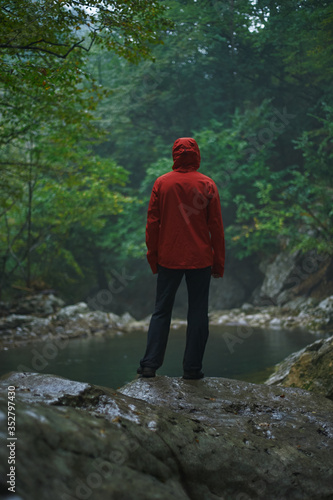 Hiker from behind standing in mountains in rain with backpack wearing raincoat.