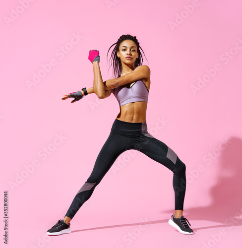 Warming up before training. Photo of sporty girl with perfect body on pink background. Strength and motivation