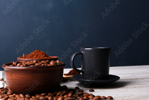 Espresso cup, roasted Arabica beans in clay bowls, coffee powder on while table against dark blue wall. Side view, copy space. Coffee shop, morning, baristas workplace concept