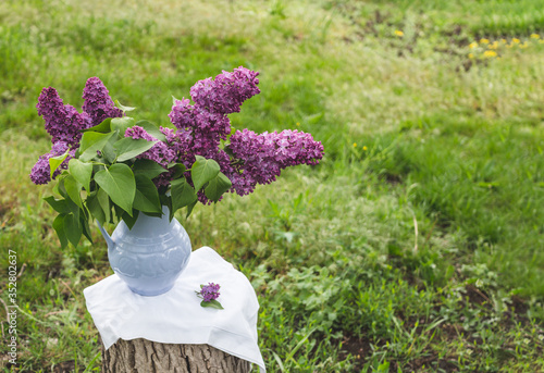 Spring background in a garden. Lilac flowers in old blue porcelain vase or decanter on a wooden stump.